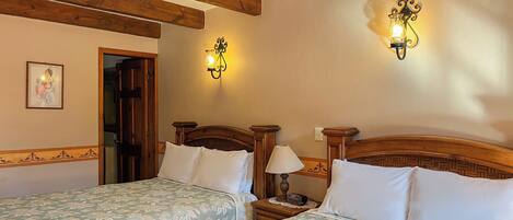 A hotel room with two single beds, wooden headboards, a nightstand with a lamp, and wall-mounted sconces.