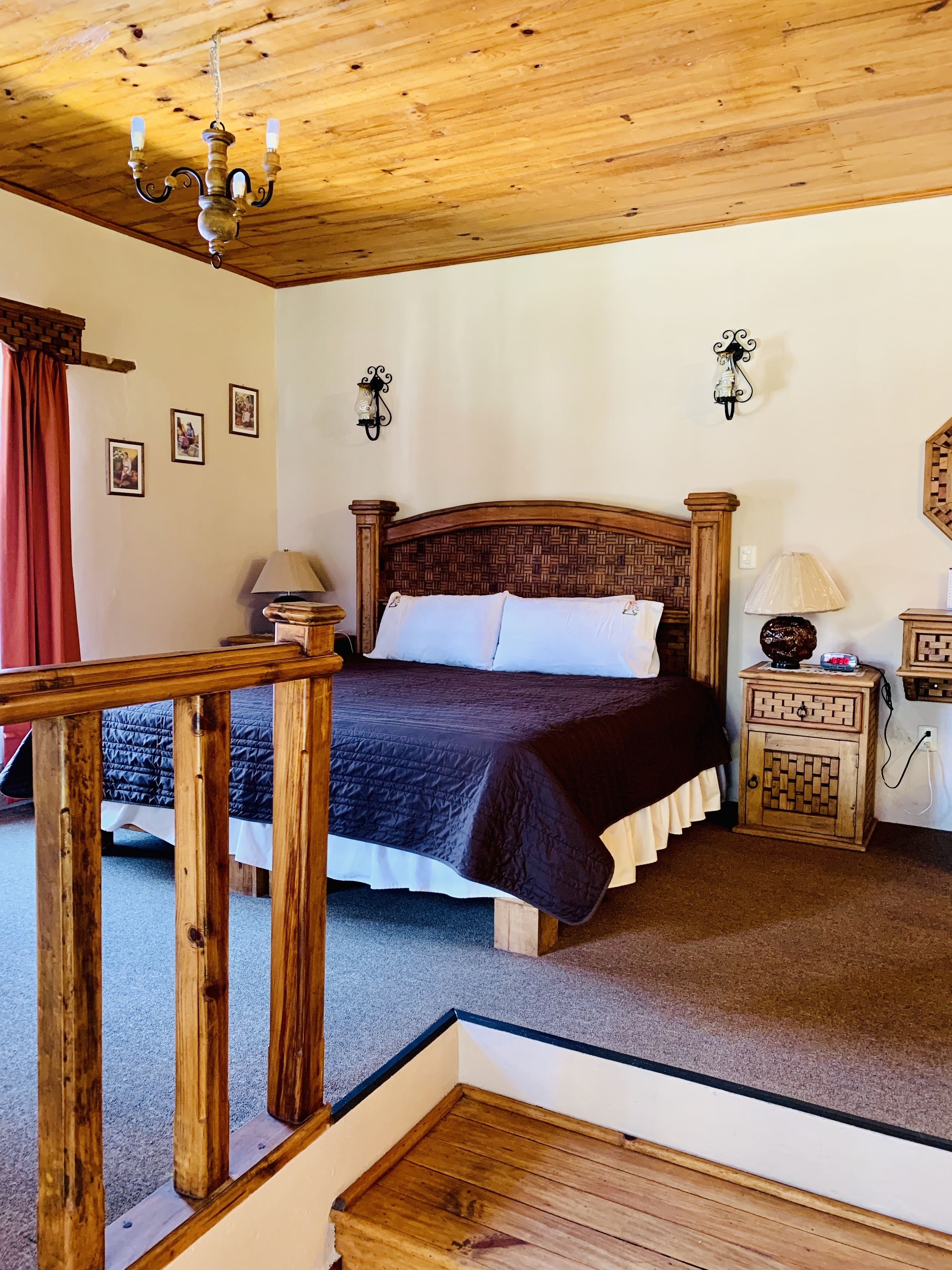 A bedroom with a wooden bed, a nightstand, a lamp, and a chandelier.