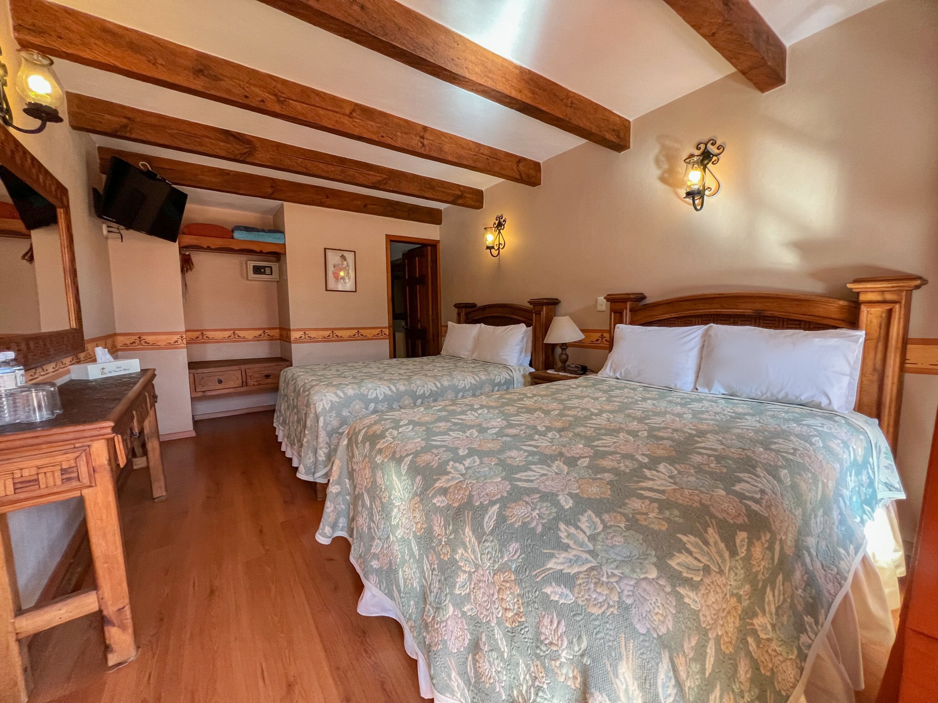 Una habitación con dos camas, vigas de madera, un escritorio y un espejo.