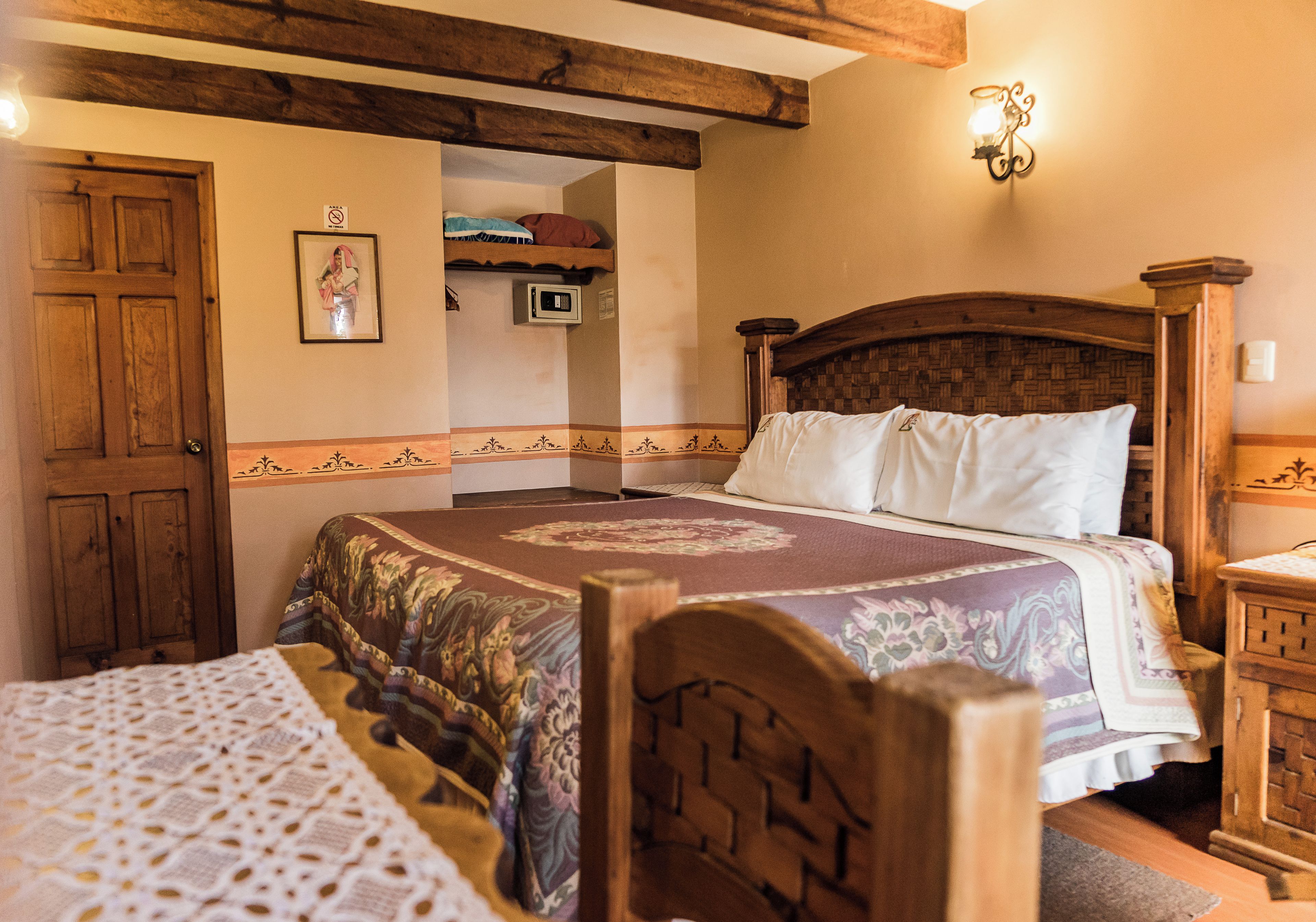 A bedroom with a wooden bed, a wooden headboard, a bedside table, and a wall-mounted light fixture.