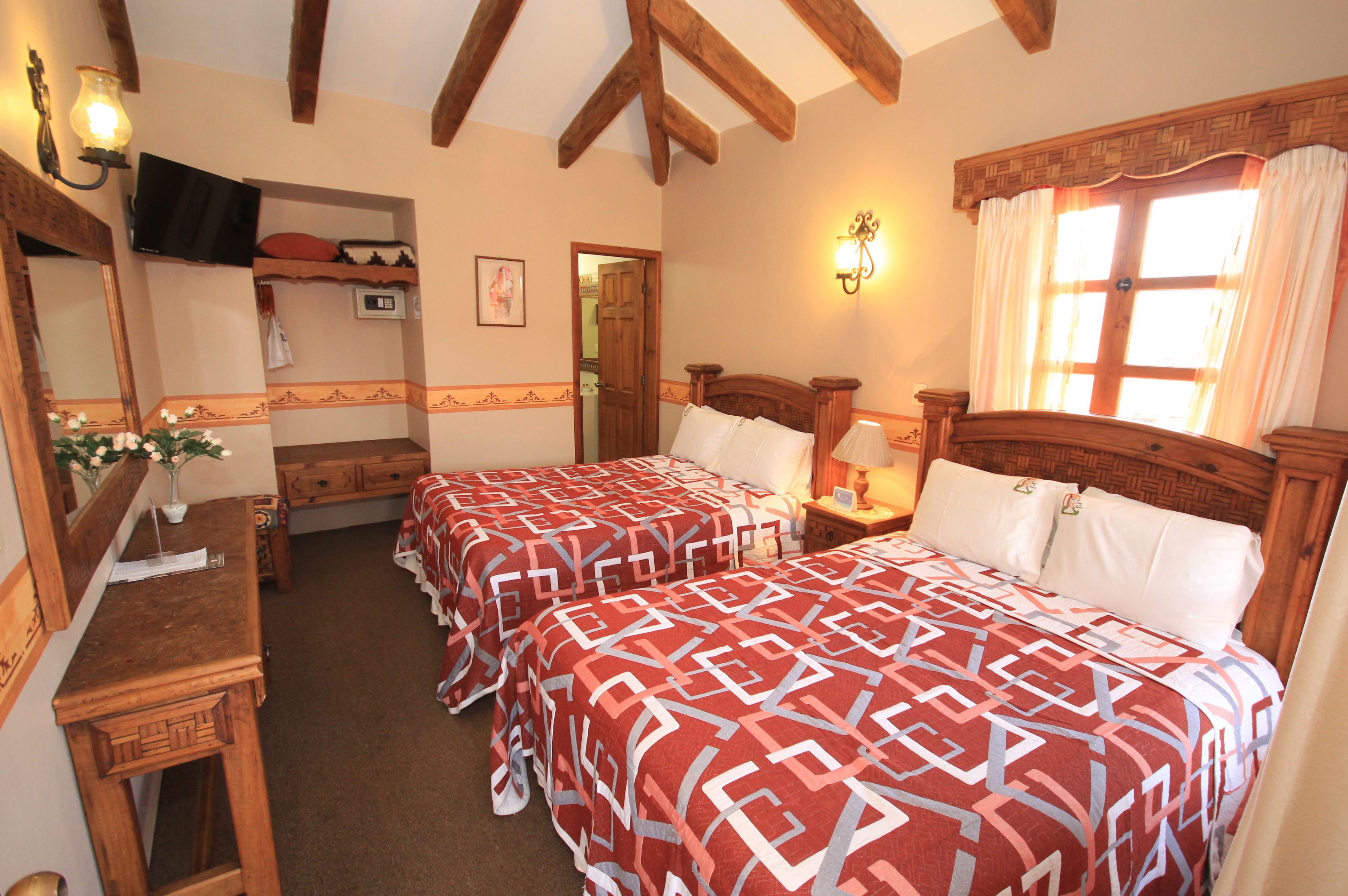 A bedroom with two beds, wooden furniture, a TV, and a window with curtains.