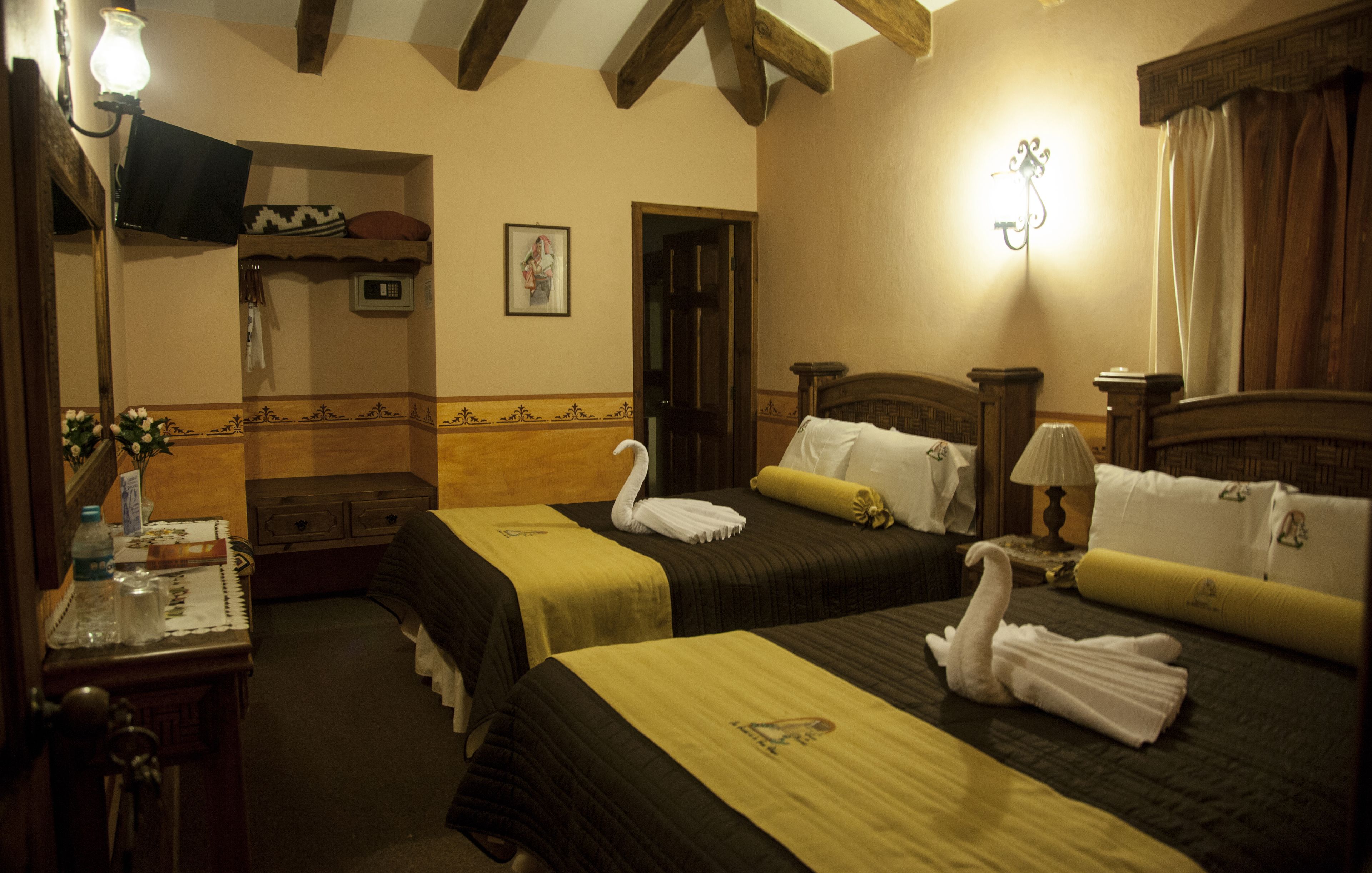 A hotel room with two beds, wooden headboards, and a small table with a lamp.