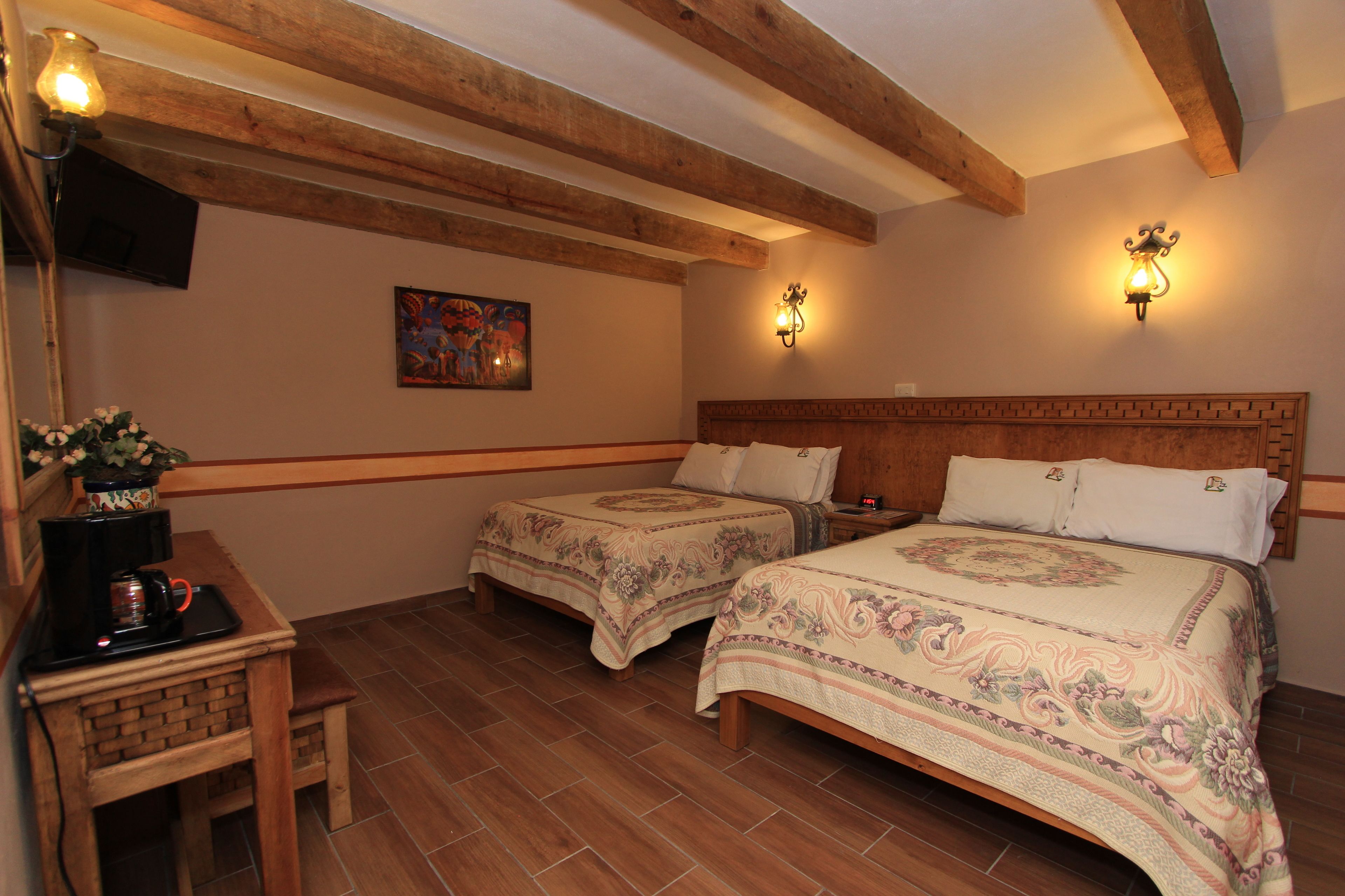 Un dormitorio con dos camas, vigas de madera, una zona de café y luces fijadas a la pared.