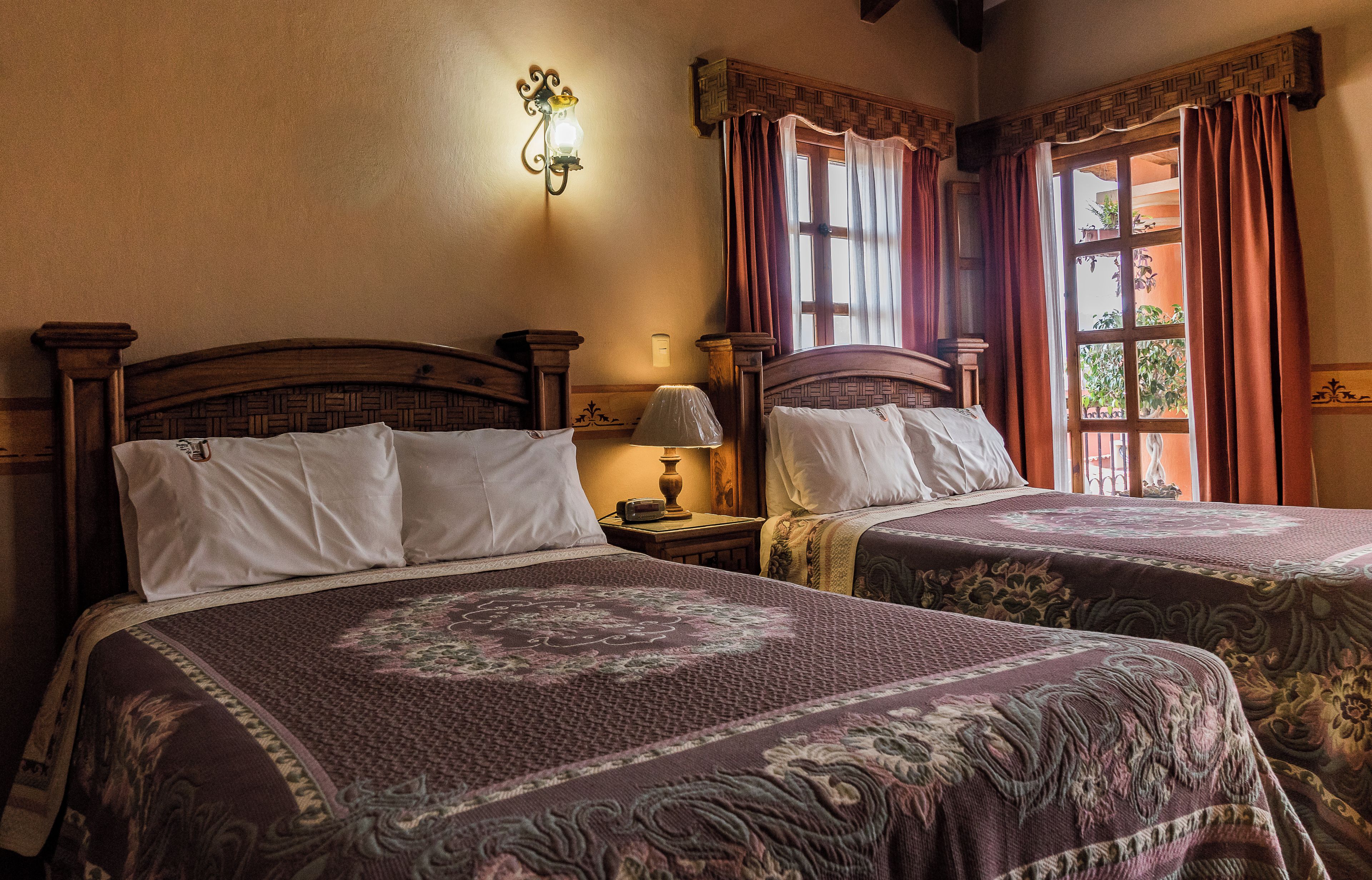 A room with two beds, each with a headboard, a bedside table with a lamp, and a wall-mounted light fixture.
