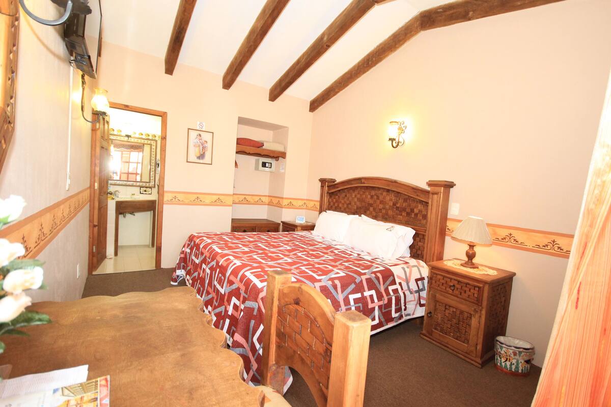 A bedroom with a wooden bed, a nightstand with a lamp, a mirror, and a wall-mounted light fixture.