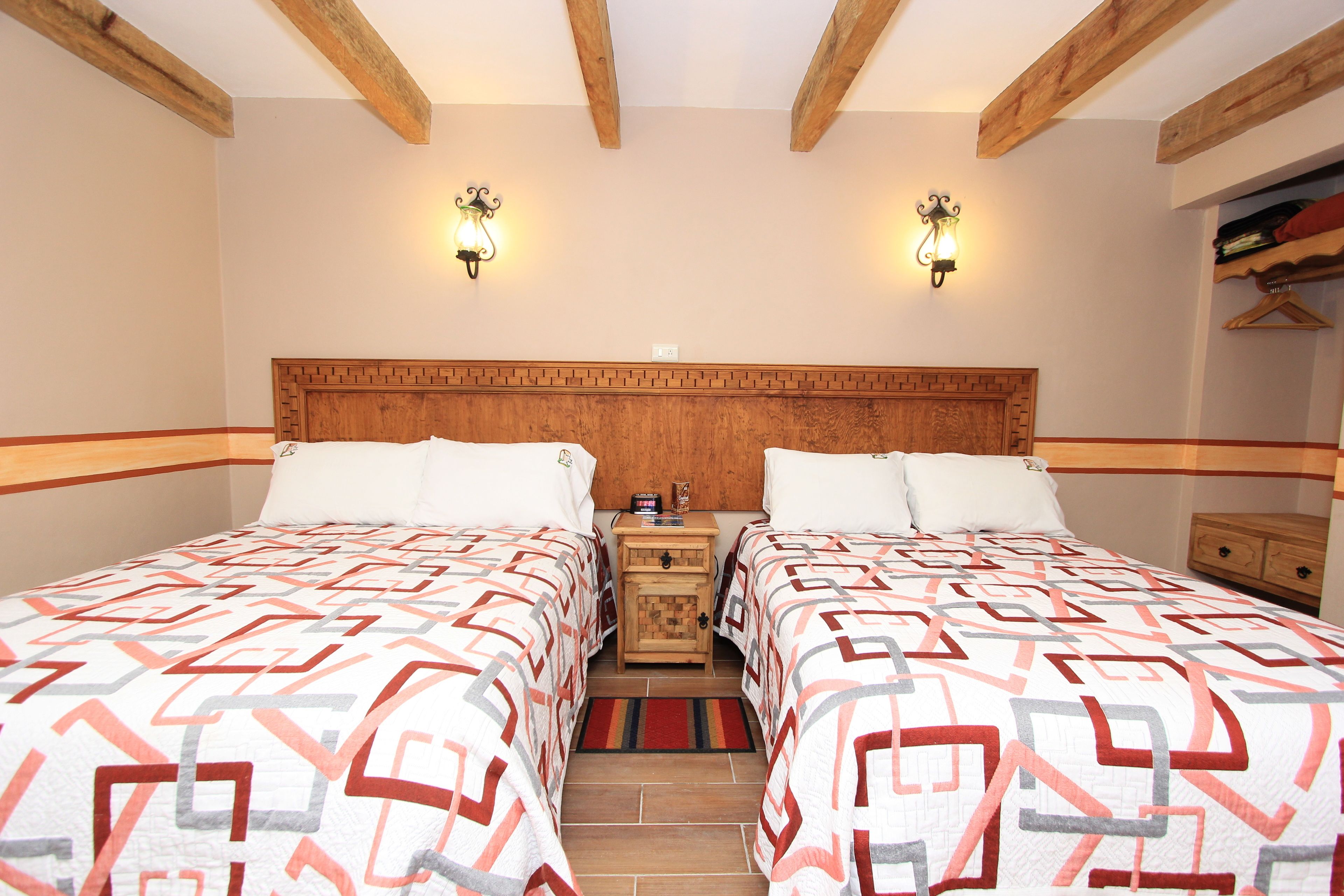 Habitación doble con dos camas, cabecero de madera, mesitas de noche y lámparas de pared.