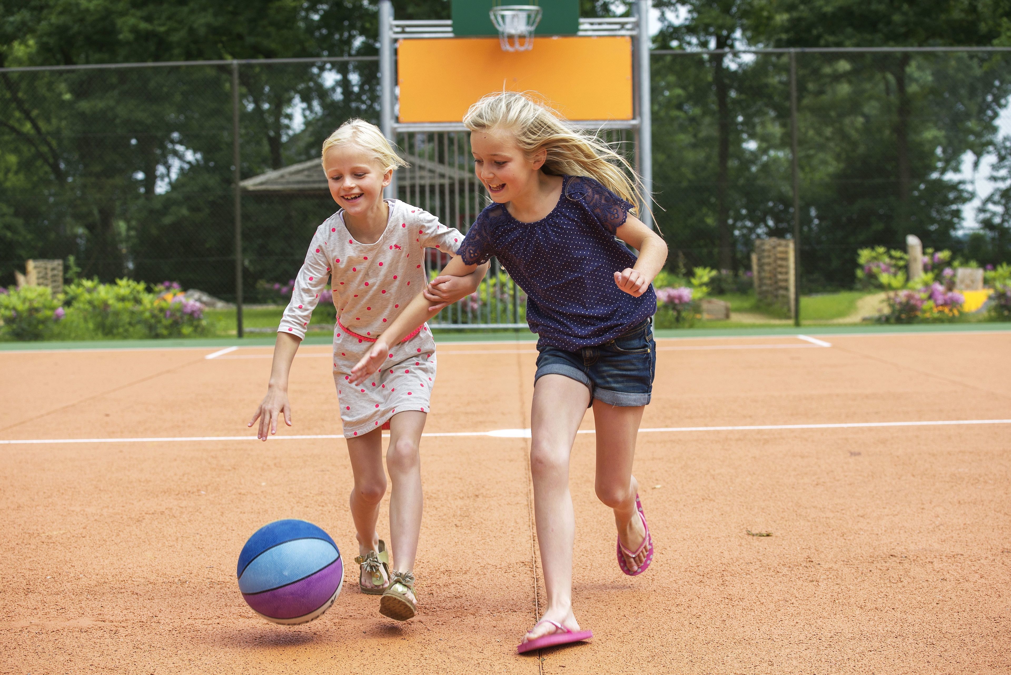 Zwei Kinder spielen mit einem Ball auf einem Sandplatz.