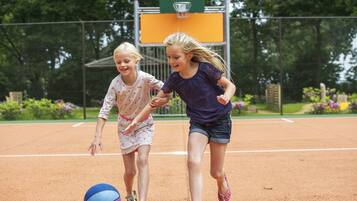 Two children playing with a ball on a clay tennis court.