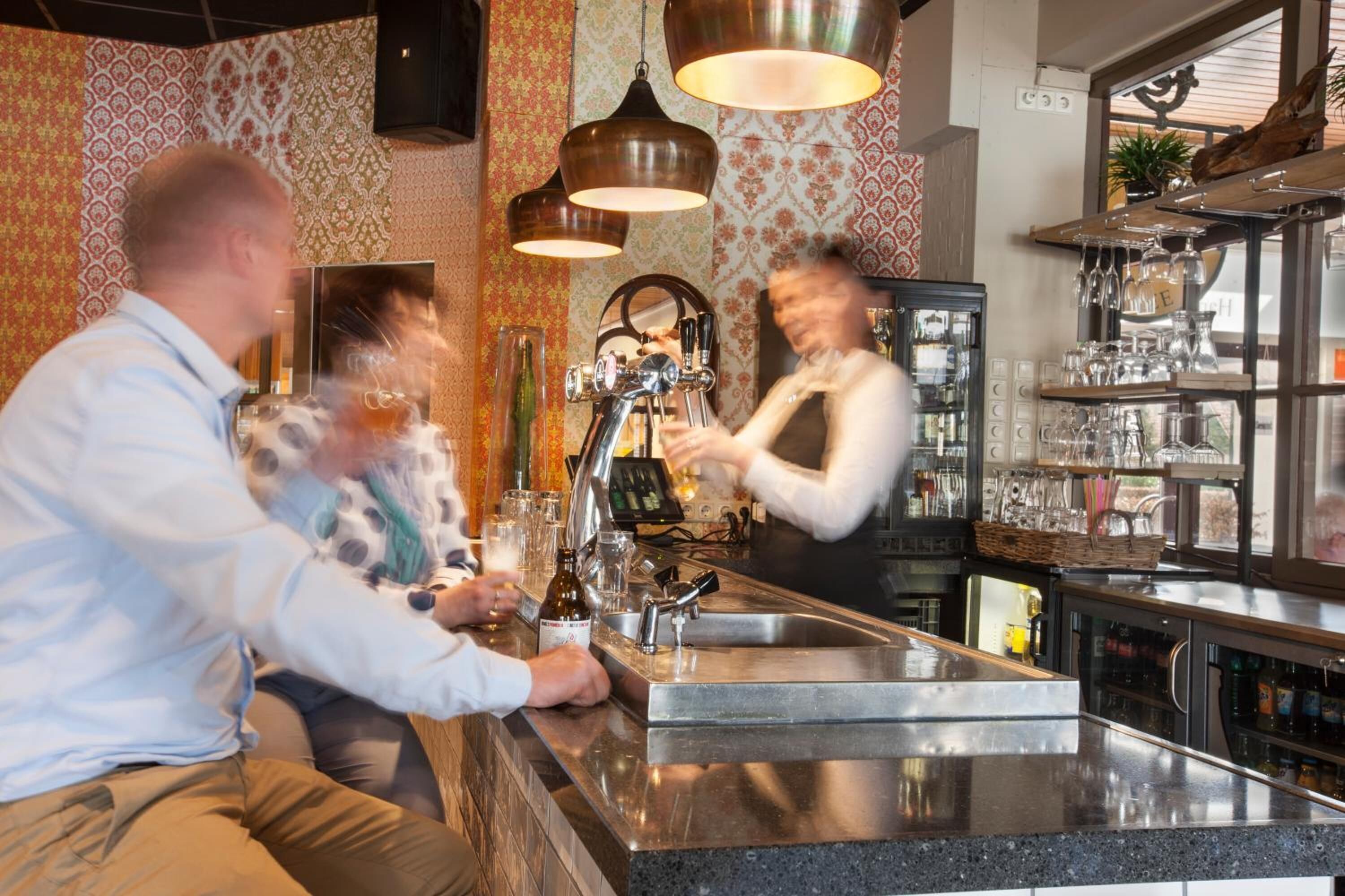 Una zona de bar con mostrador de acero inoxidable, taburetes y lámparas colgantes.
