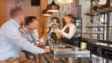 Una zona de bar con mostrador de acero inoxidable, taburetes y lámparas colgantes.