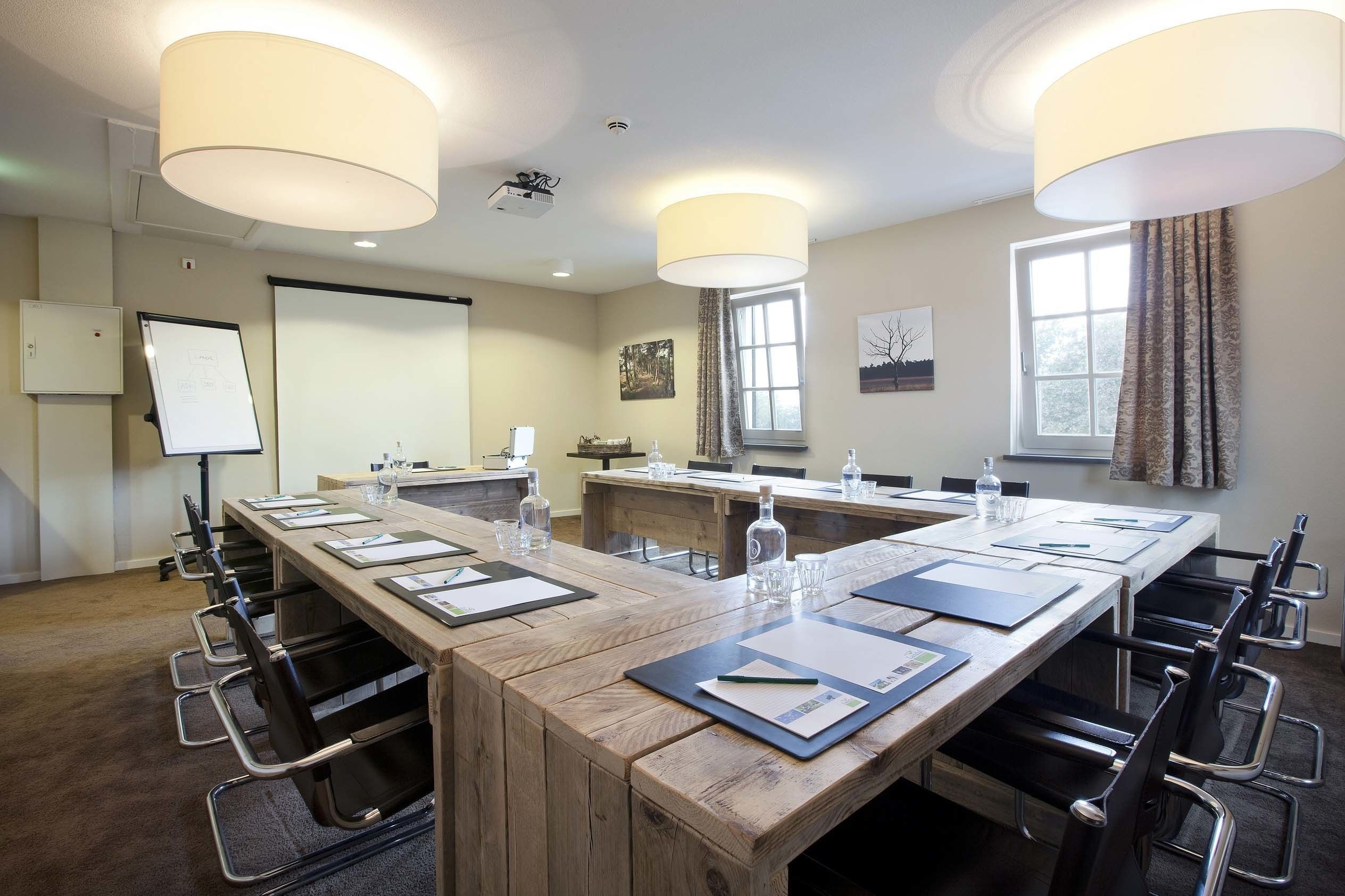 Une salle de conférence avec une longue table en bois, des chaises noires, un tableau blanc et un projecteur.