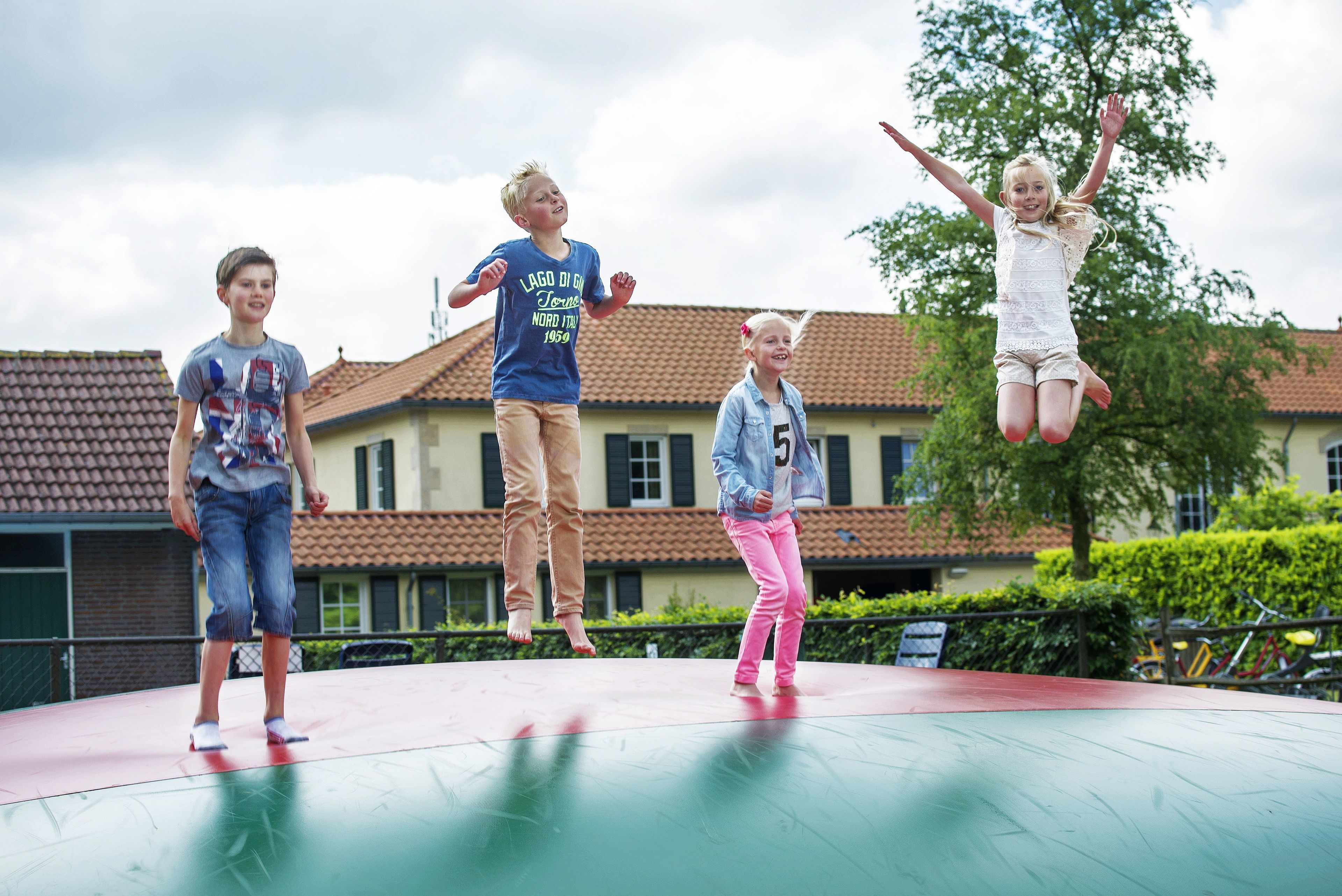 A group of children jumping on a trampoline in front of a building with a tiled roof.