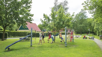 A playground with swings, climbing structures, and a red-roofed building in the background.