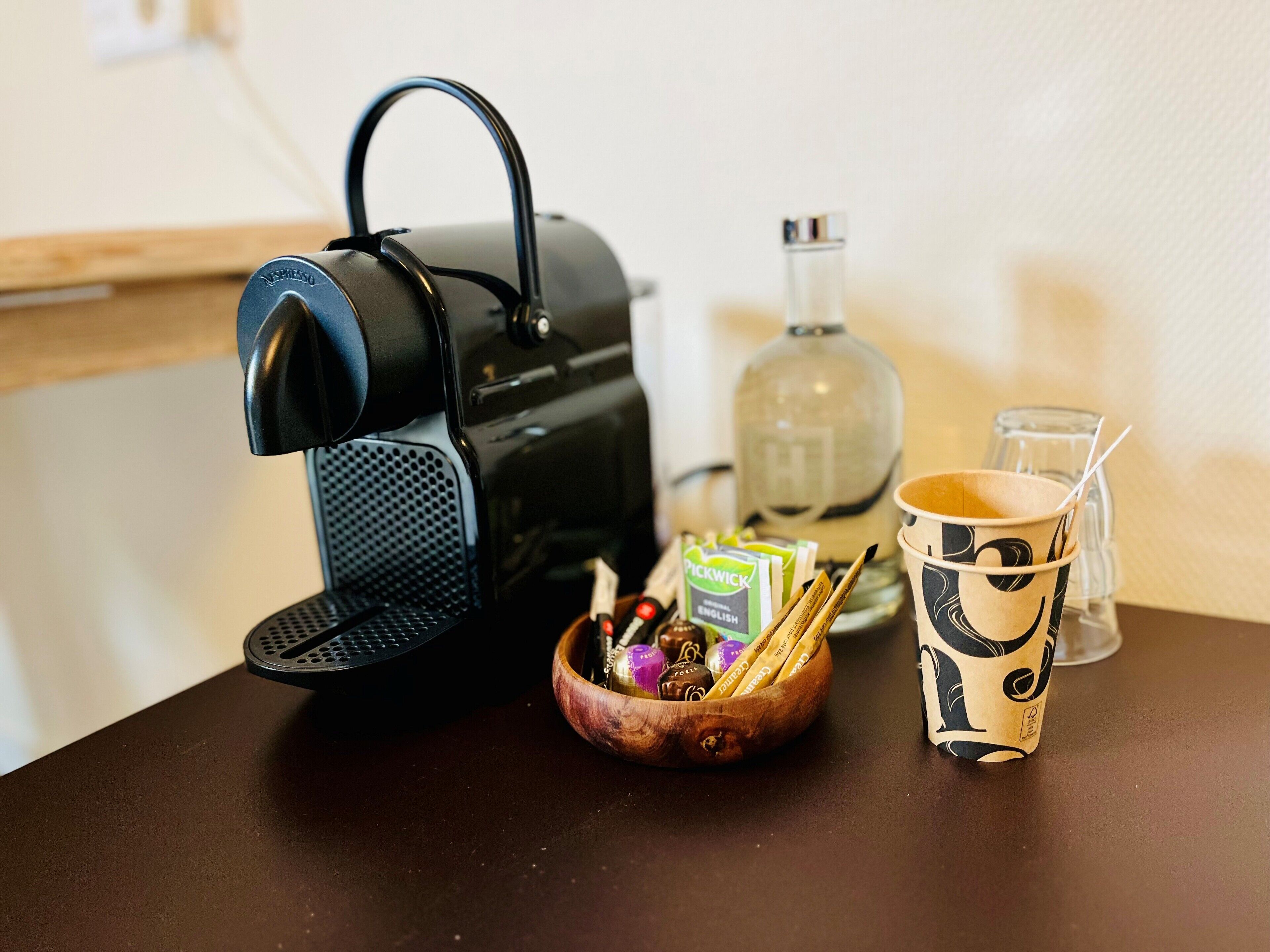 A coffee maker, a bottle, a cup, and a bowl with snacks on a table.