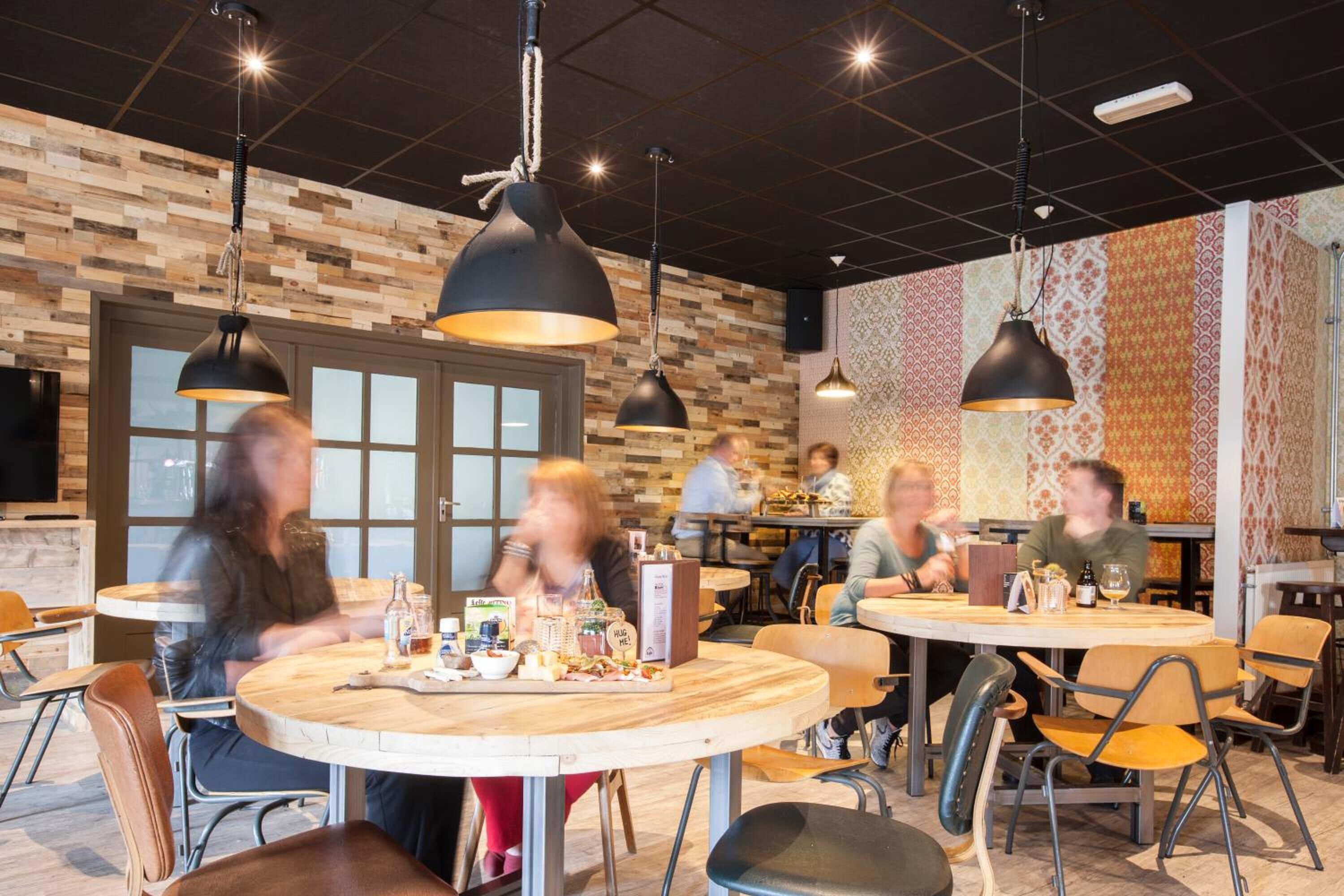 A restaurant with round tables and black pendant lighting.
