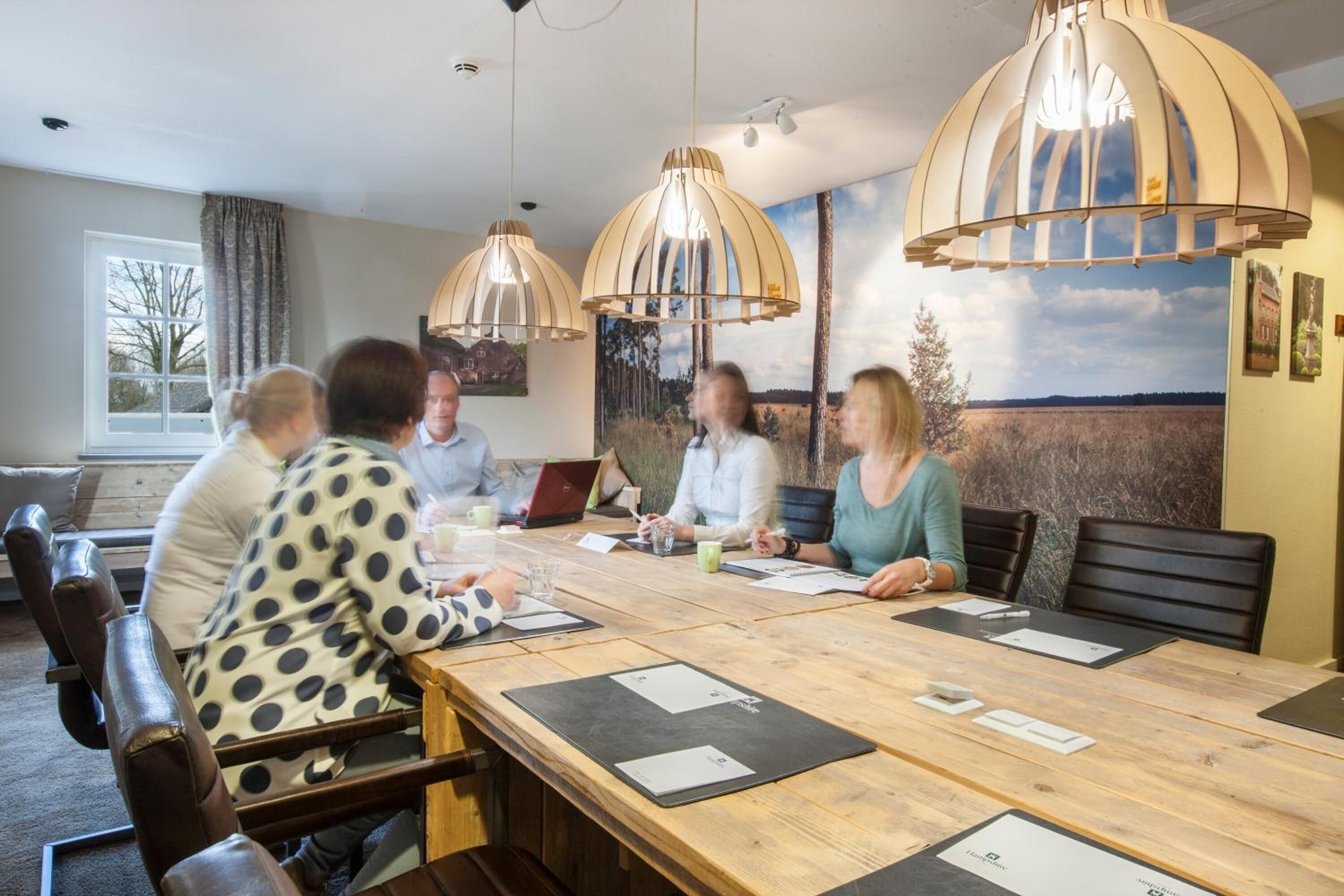 A conference room with a long wooden table, leather chairs, and pendant lighting.