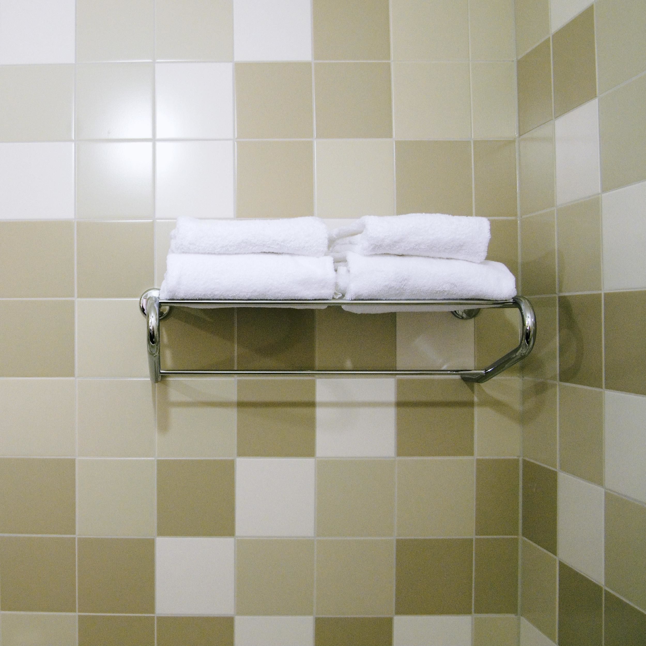 A bathroom with a towel rack holding two folded white towels. The walls are tiled with a checkered pattern in beige and white.