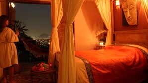 A bedroom with a bed, a nightstand, a fruit bowl, and a view of a cityscape at night. - Gavea Tropical Boutique Hotel (Rio de Janeiro)