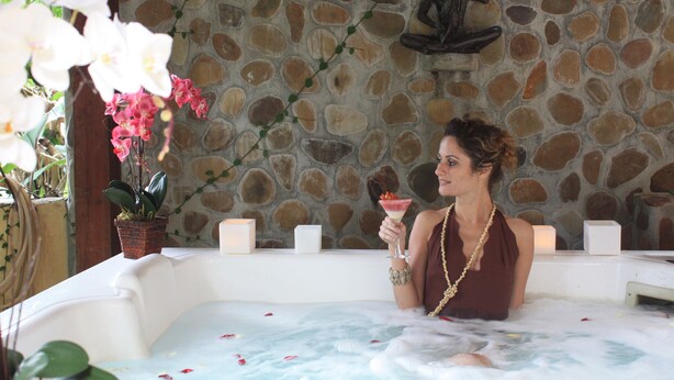 A woman in a hot tub with a stone wall background, holding a drink. - Gavea Tropical Boutique Hotel (Rio de Janeiro)