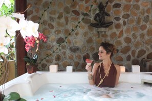 A woman in a hot tub with a stone wall background, holding a drink. - Gavea Tropical Boutique Hotel (Rio de Janeiro)