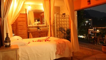 A bedroom with a large bed, a bathroom with a sink and mirror, and a balcony with a table and chairs.