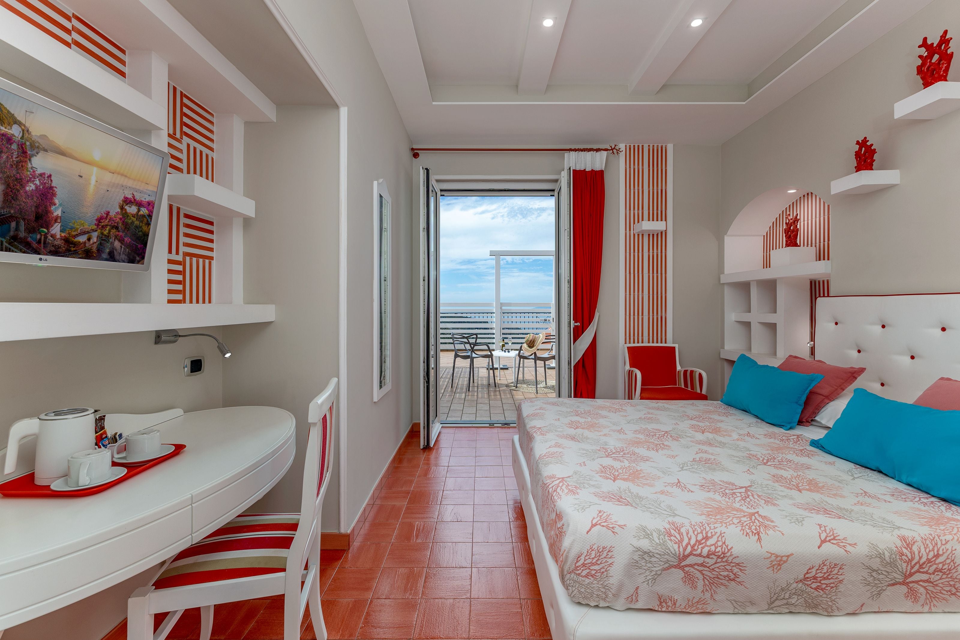 Habitación de hotel con cama, escritorio, silla, balcón y cortina a rayas rojas y blancas.