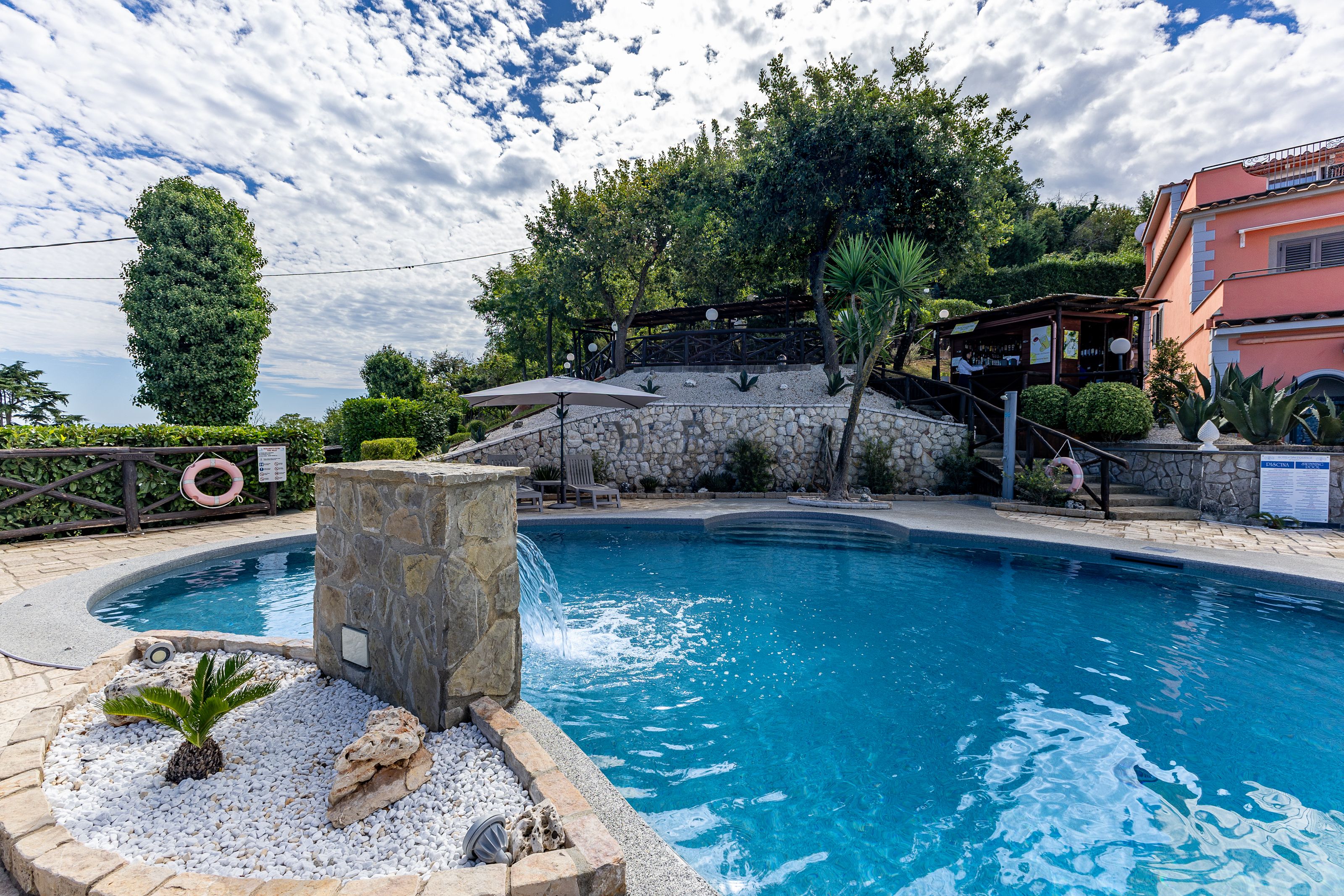 Une piscine avec un mur en pierre, une bouée de sauvetage et un espace bar doté de sièges en plein air.