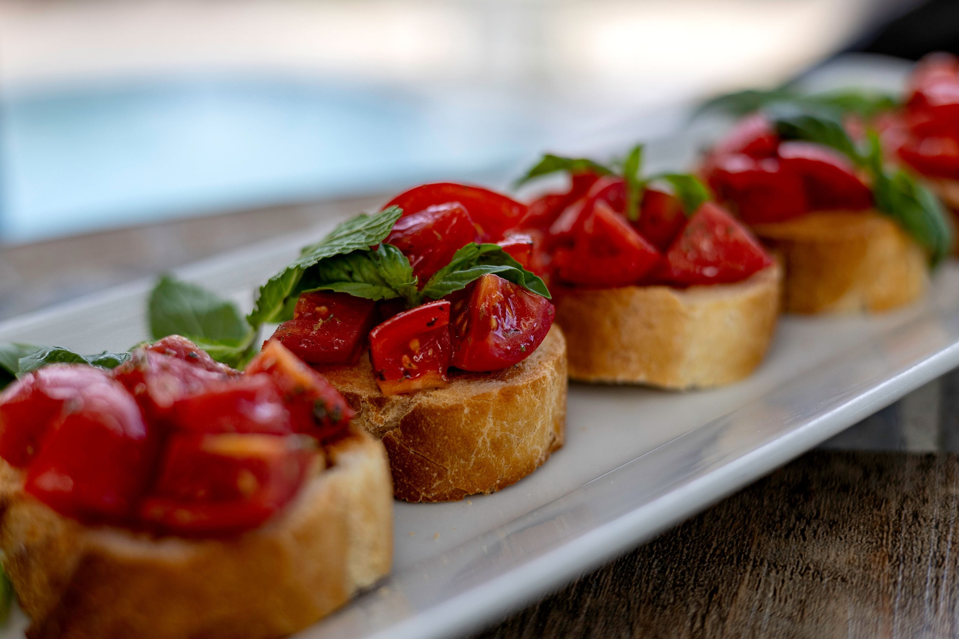 A white rectangular plate with several pieces of bruschetta topped with tomatoes and basil.