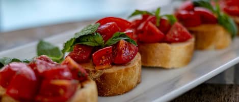 A white rectangular plate with several pieces of bruschetta topped with tomatoes and basil.