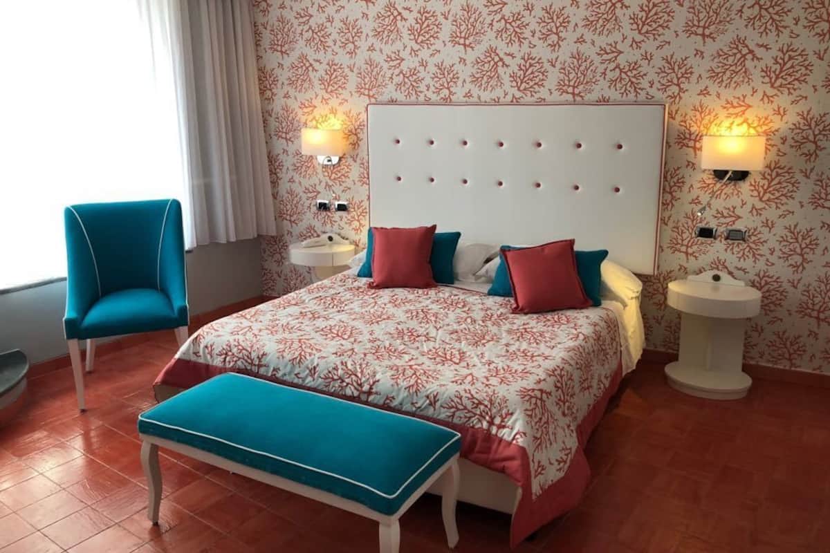 A hotel room with a bed, two bedside tables, a nightstand, a chair, and a bench.