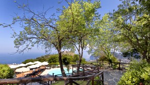 Área de piscina com guarda-sóis e espreguiçadeiras, cercada por árvores e com vista para a costa.