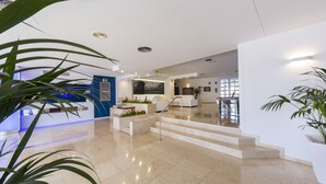 Un vestíbulo amplio con suelo de mármol, un mostrador de recepción, una escalera y plantas en macetas.