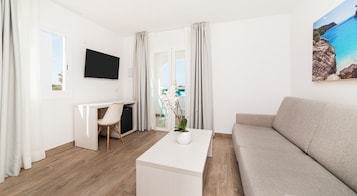 A modern living room with a sofa, a white coffee table, a desk with a chair, and a TV mounted on the wall.