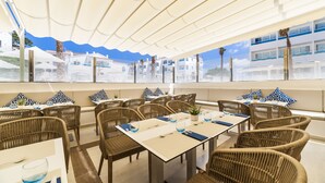 Un restaurante con mobiliario de mimbre, mesas blancas y cojines de estampado azul.