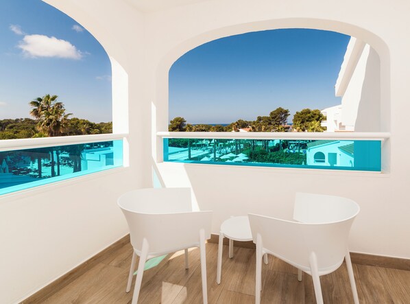Una habitación con piscina, mobiliario blanco y vistas al mar y vegetación.