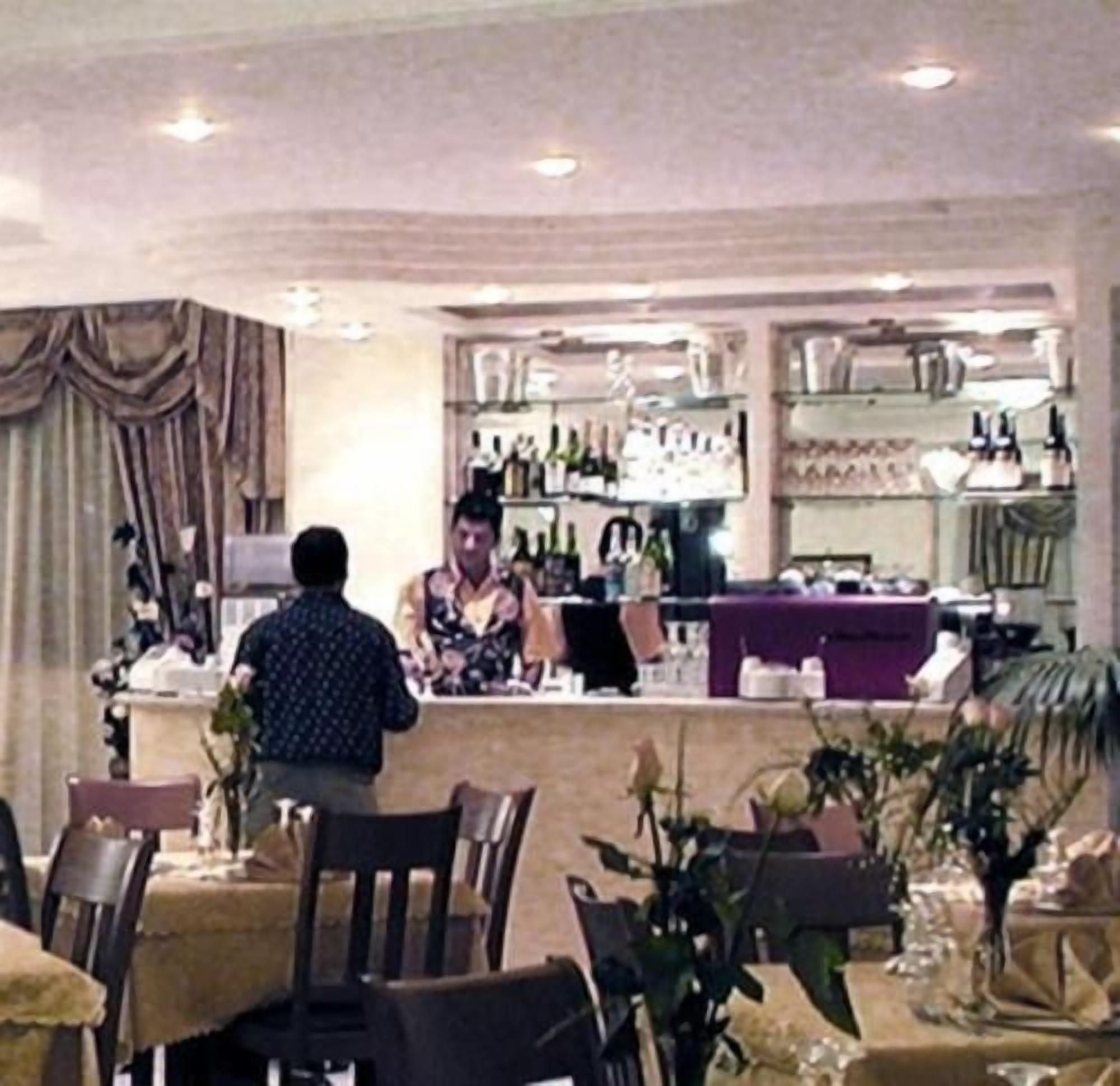 L’intérieur d’un restaurant, avec des tables, des chaises, un comptoir et des étagères remplies de bouteilles.