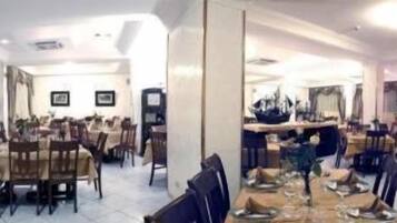 Un comedor espacioso con varias mesas y sillas, una columna central y cuadros en las paredes.