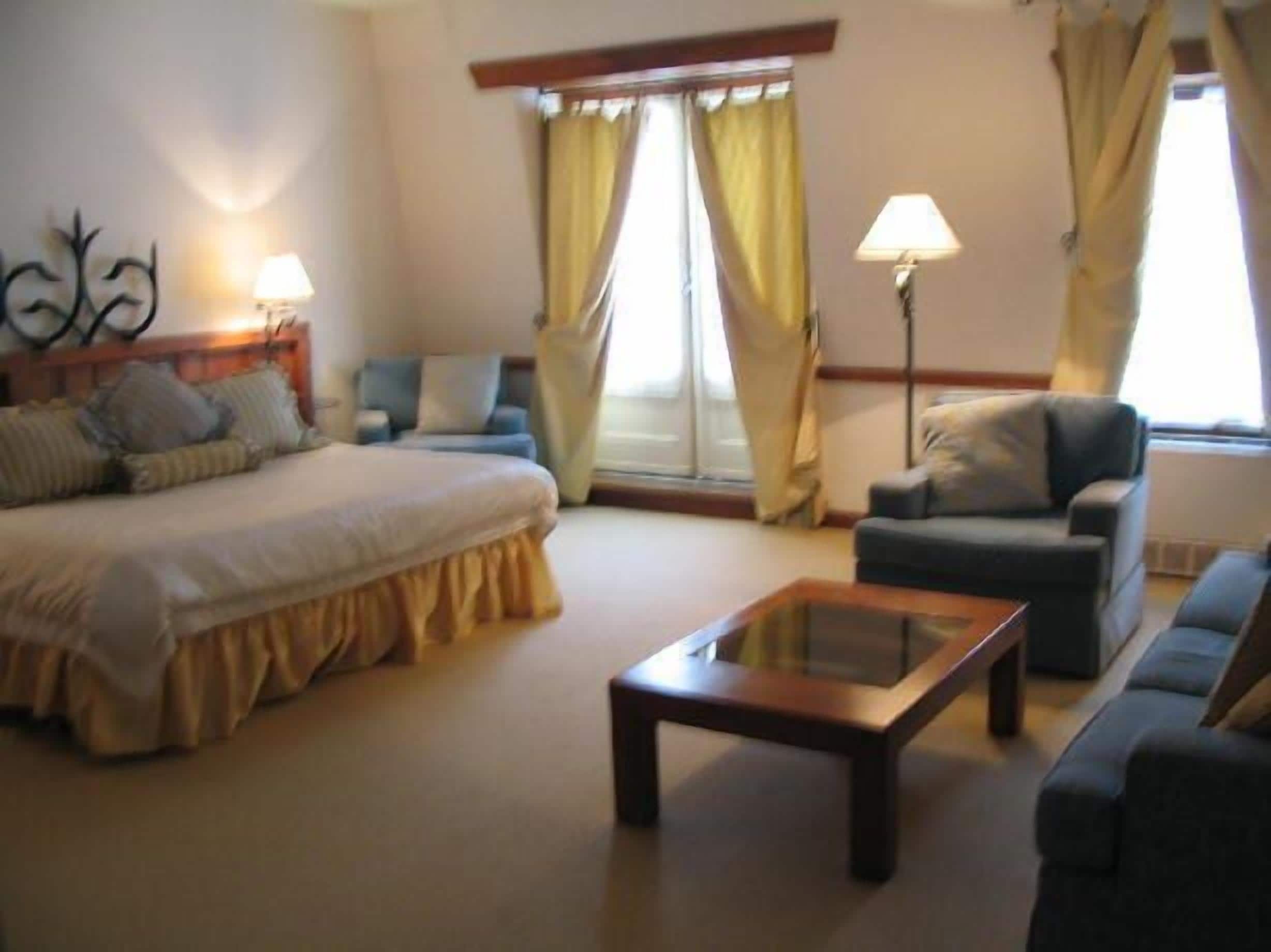 Habitación de hotel con cama, sofá, sillón, mesita de centro y dos lámparas.
