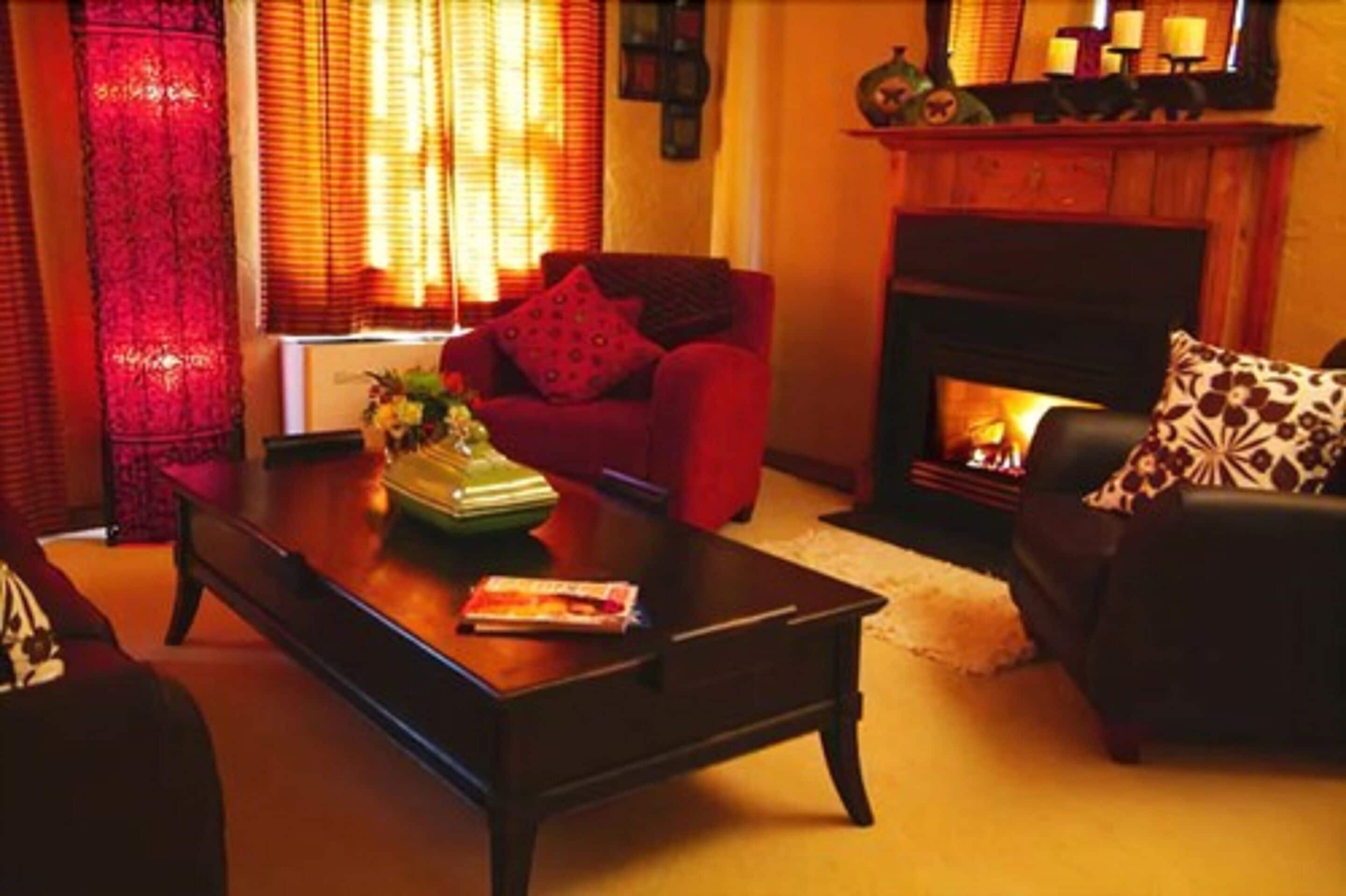 A cozy living room with a fireplace, red sofa, and a coffee table with a vase and book.