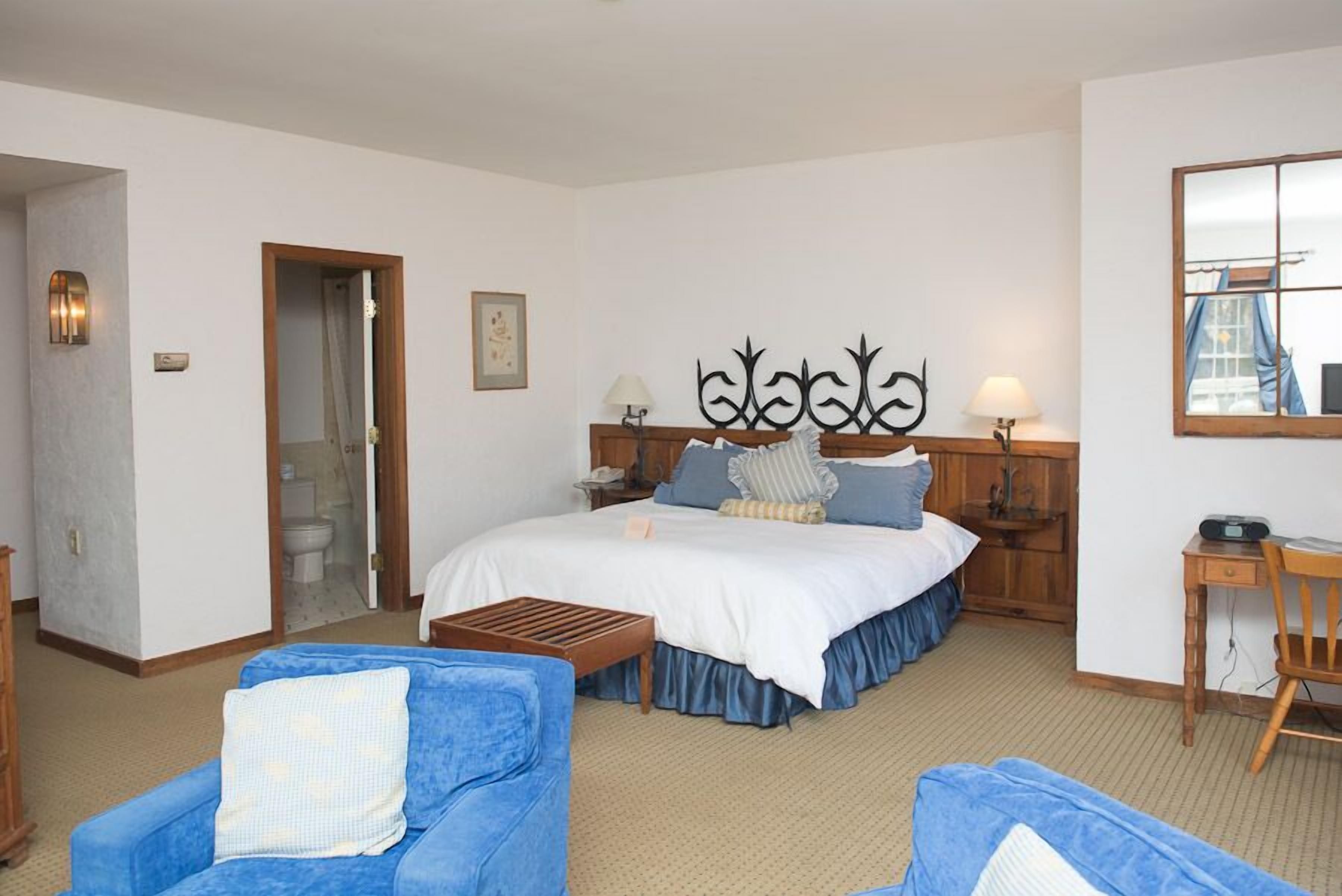 Une chambre d’hôtel avec un grand lit, deux tables de chevet, un bureau et deux fauteuils bleus.
