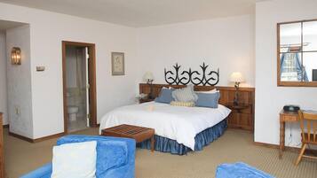 Une chambre d’hôtel avec un grand lit, deux tables de chevet, un bureau et deux fauteuils bleus.