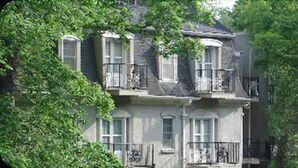 Un bâtiment à deux étages, doté d’un balcon au deuxième étage, et entouré d’arbres.