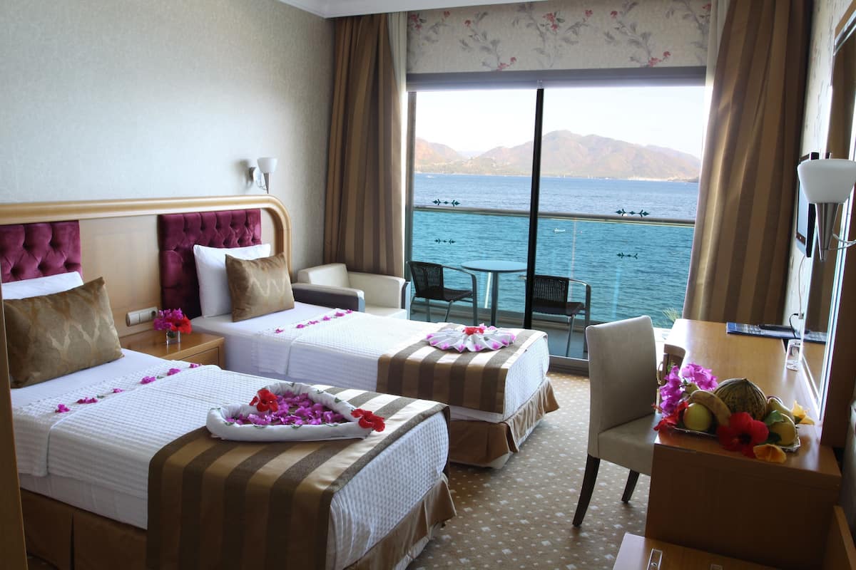 A hotel room with two beds, a balcony with a view of the sea, and a dining area.