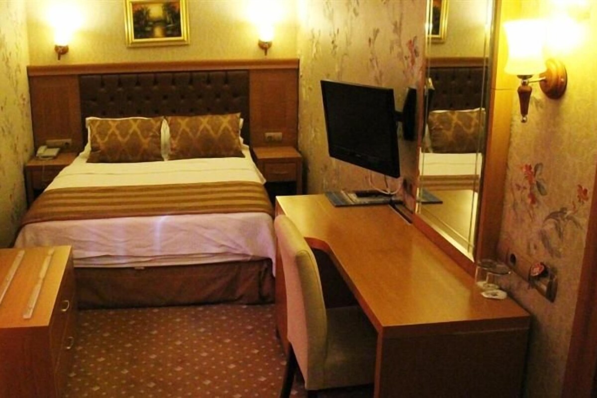 Una habitación de hotel con cama, mesita de noche, escritorio, silla y televisor.