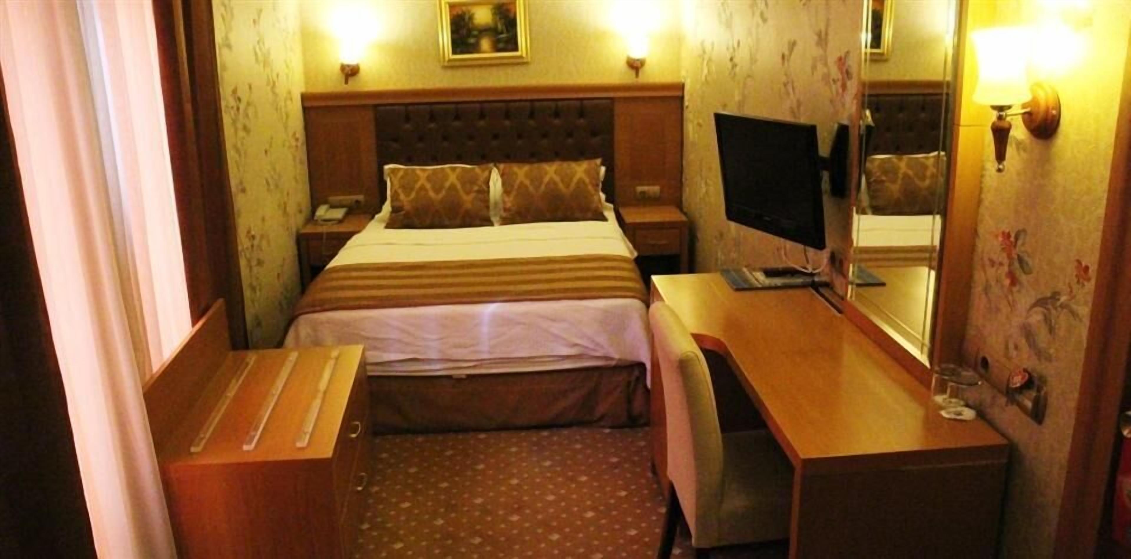 Una habitació d'hotel amb un llit, taules de nit, escriptori, cadira, televisió i mirall.