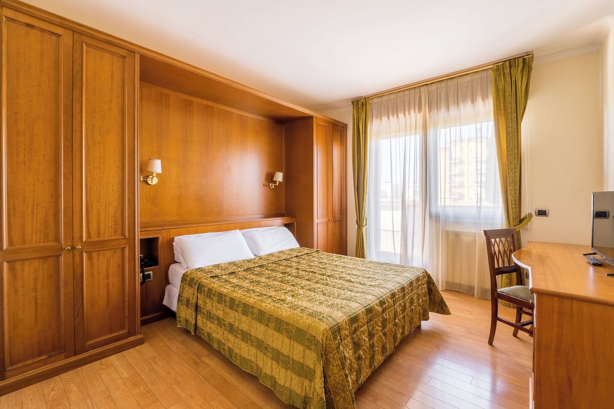 A bedroom with a bed, wooden wardrobe, desk, and chair.