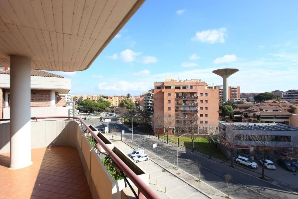 En balkon med udsigt over bybilledet, inklusive en høj bygning og en gade med parkerede biler.