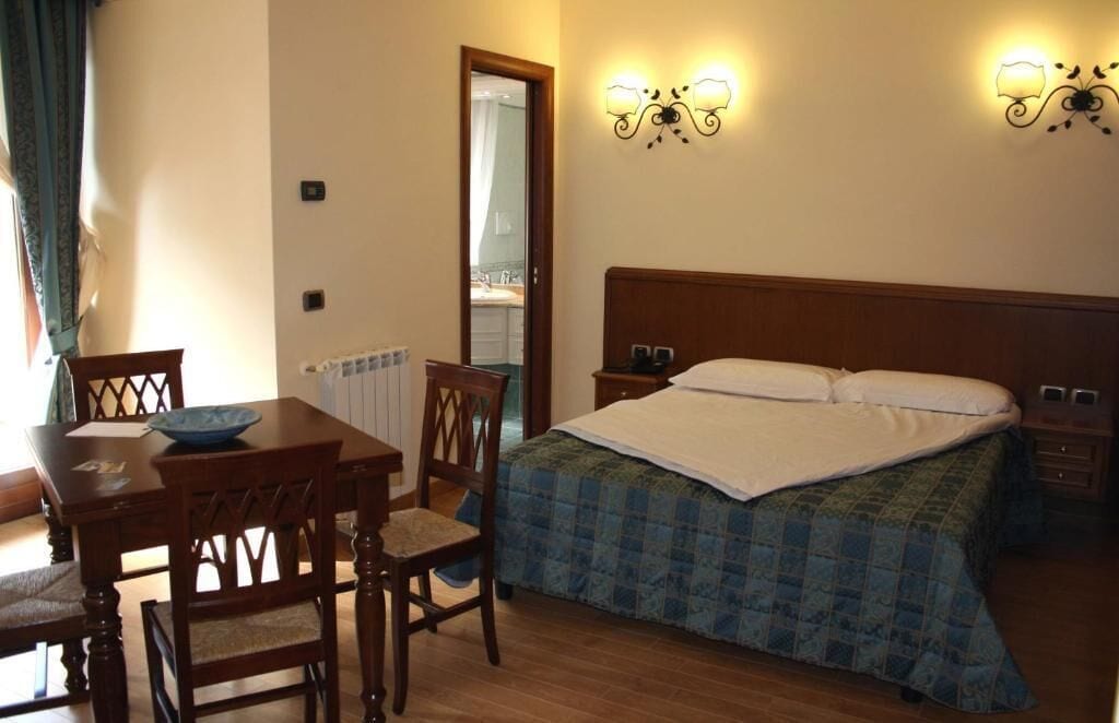 A bedroom with a wooden bed, a bedside table, a nightstand, a chair, a table with a bowl, and two wall-mounted lamps.