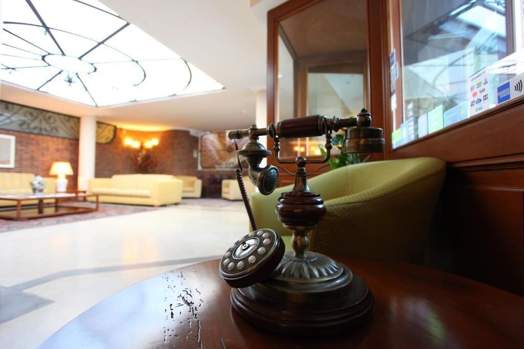 A vintage rotary telephone on a wooden table in a well-lit room with a large window, a sofa, and a lamp.