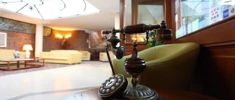A vintage rotary telephone on a wooden table in a well-lit room with a large window, a sofa, and a lamp.